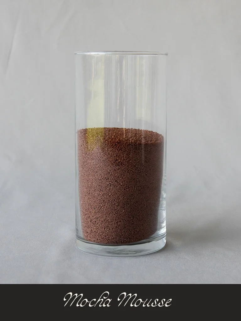 A tall glass filled with mocha mousse, which has a layered appearance with dark brown and lighter yellowish layers. The glass is placed on a white surface with a plain light background. The text "Mocha Mousse" is written below the image.