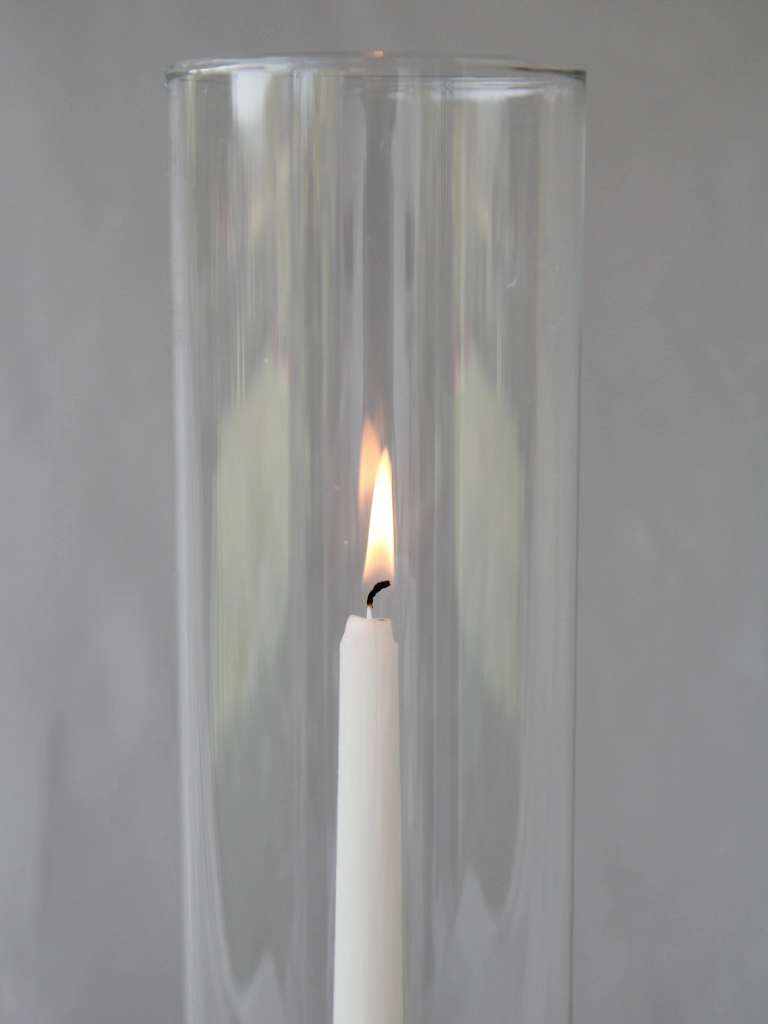A white candle burning inside a tall clear glass vase.