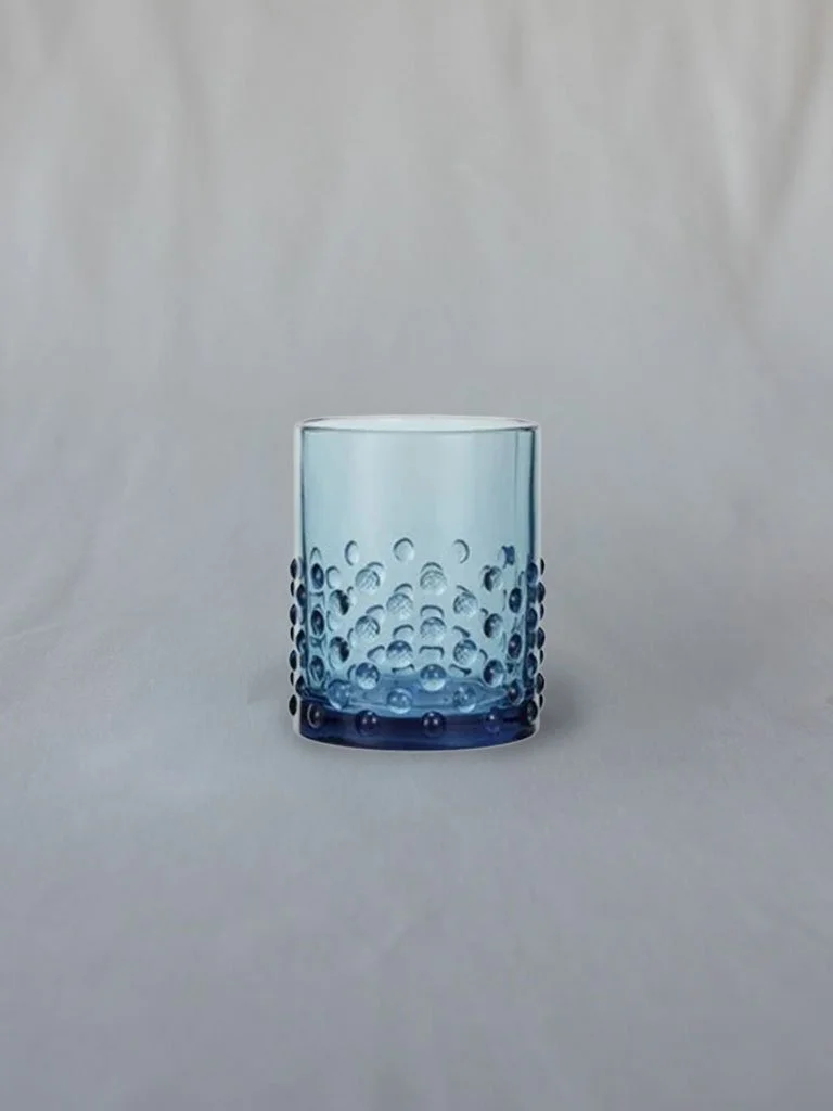 A blue glass tumbler with bubbles inside, set against a plain light background.
