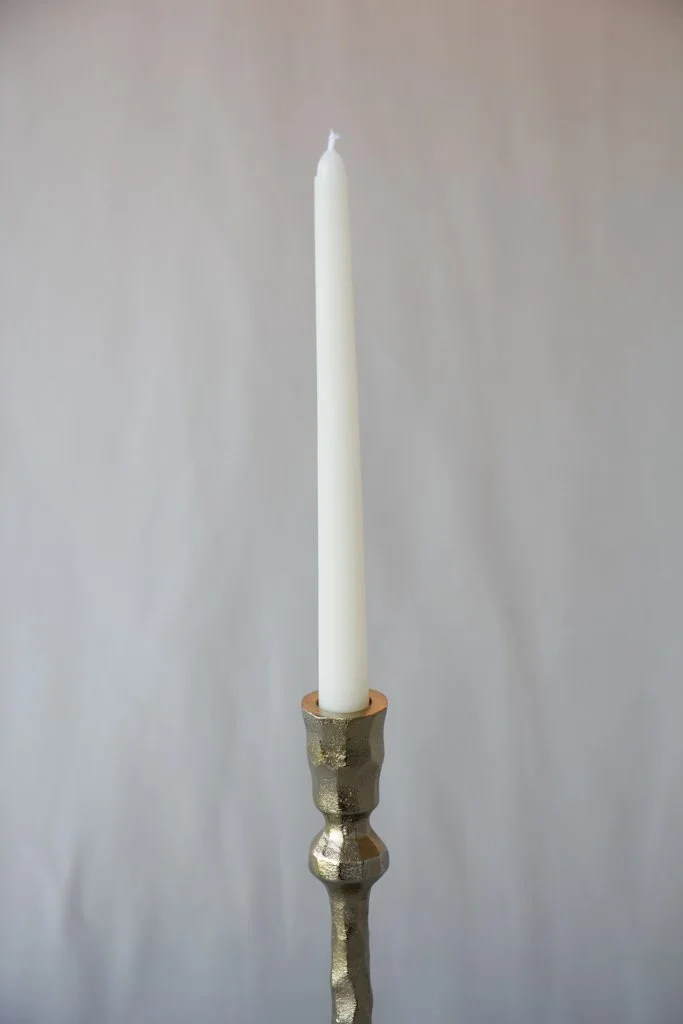 A white candle in a metallic candle holder against a plain background.
