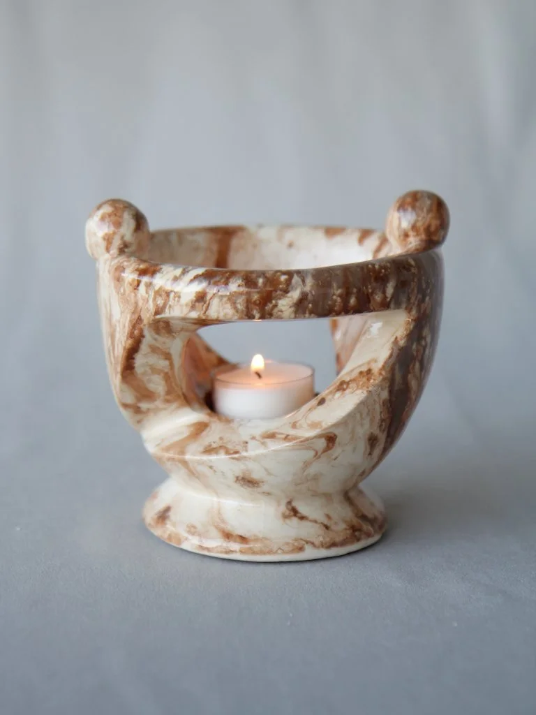 Marble candle holder with a lit tea light candle inside, set against a light gray background.