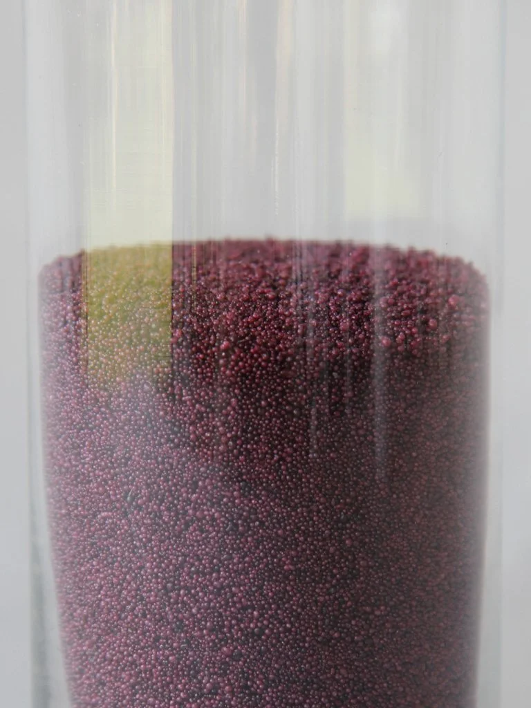 Close-up of a container filled with tiny purple and yellow beads or particles.