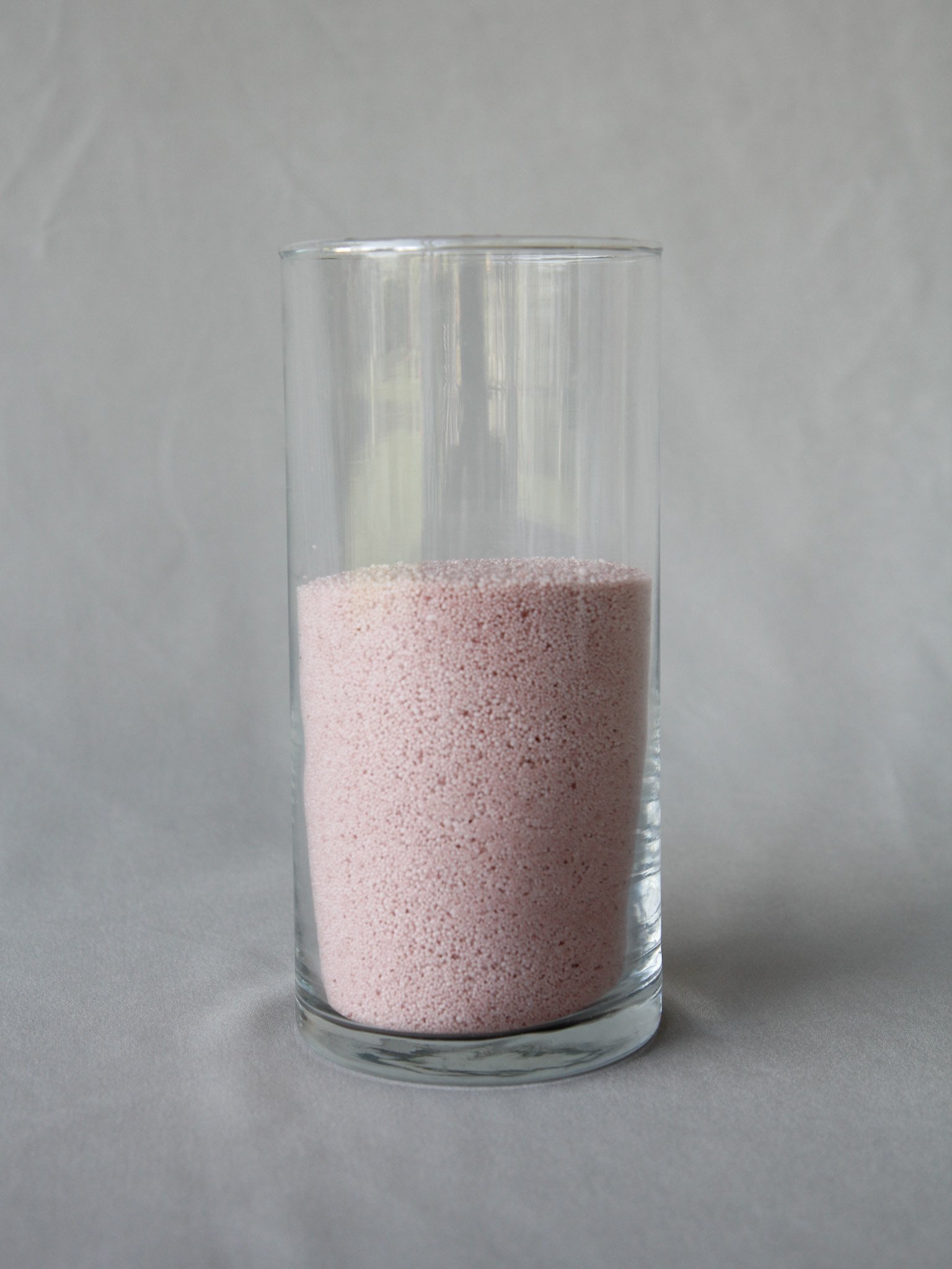 A clear glass filled with pink granular powder, set against a plain light gray background.