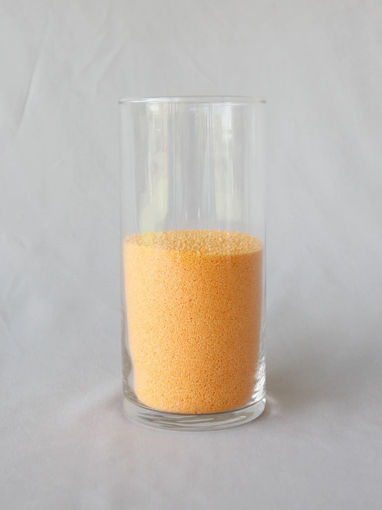 A clear glass with yellow powdered sprinkles inside, set against a plain white background.