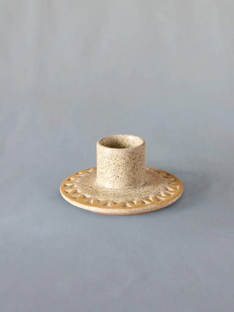 A small ceramic candle holder on a matching ceramic plate with decorative triangular patterns, against a light blue background.