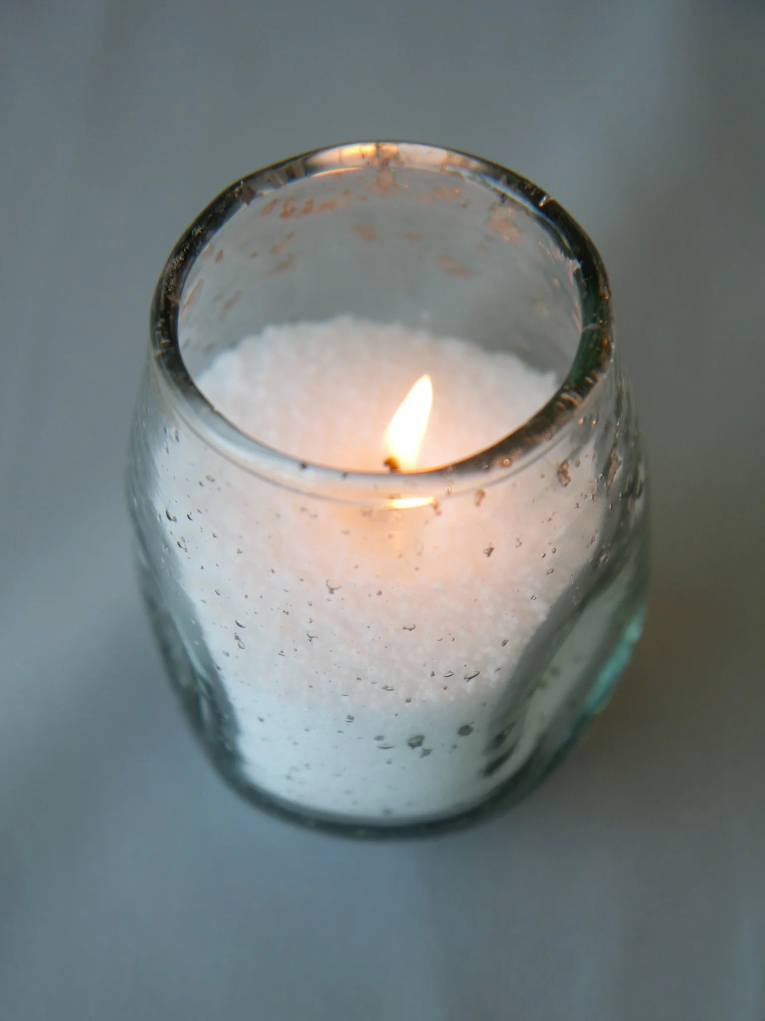 A lit candle inside a glass holder with a textured surface.