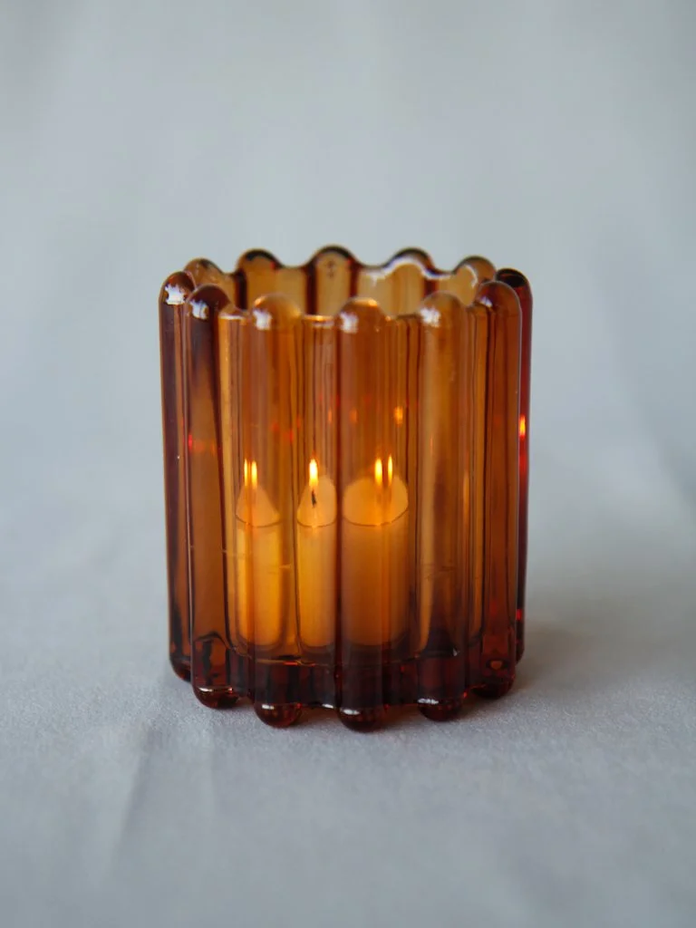 A decorative amber glass candle holder with a fluted design, illuminated from within.