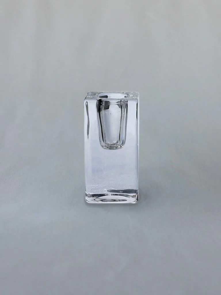 Close-up of a clear glass earring holder with a single silver stud earring displayed inside.