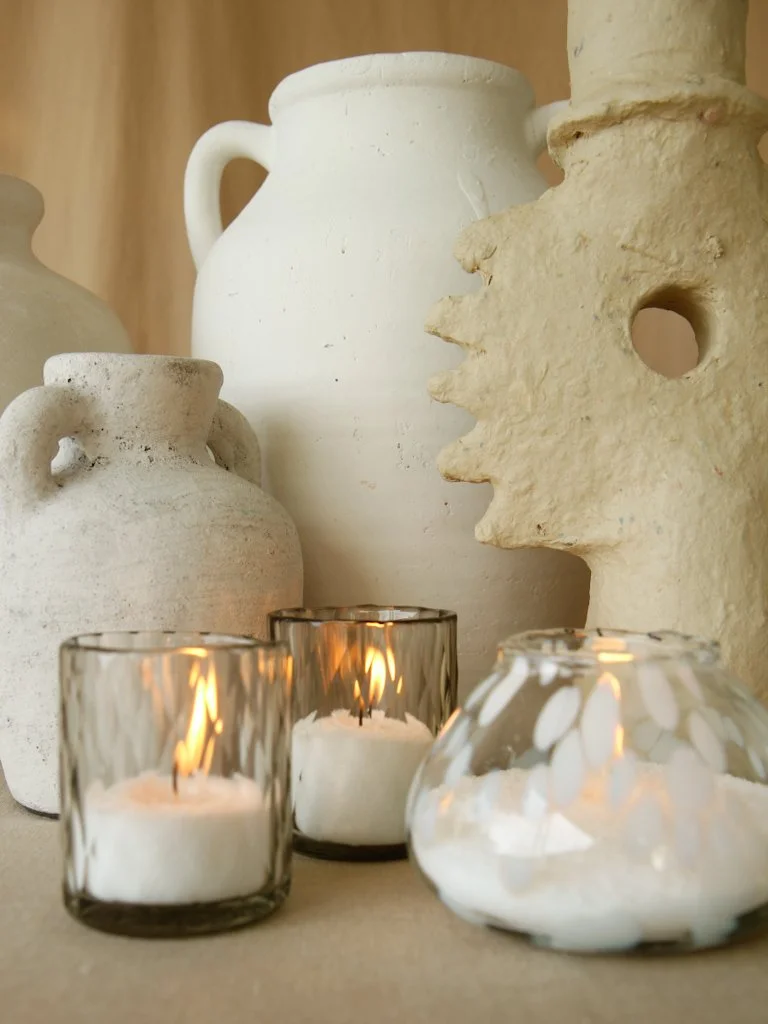 Several ceramic vases of different shapes and sizes, two lit candles in glass holders, and a small decorative glass container with white floating candles, arranged on a surface against a wooden background.