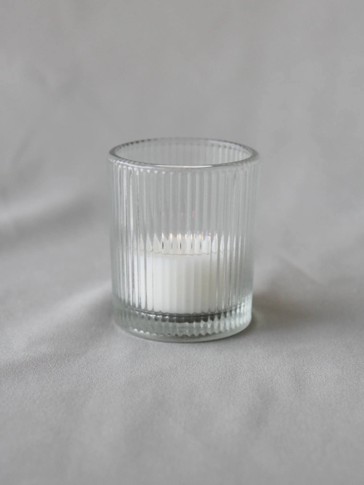 A clear glass tumbler with vertical ridges, filled with white liquid, placed on a light grey surface.