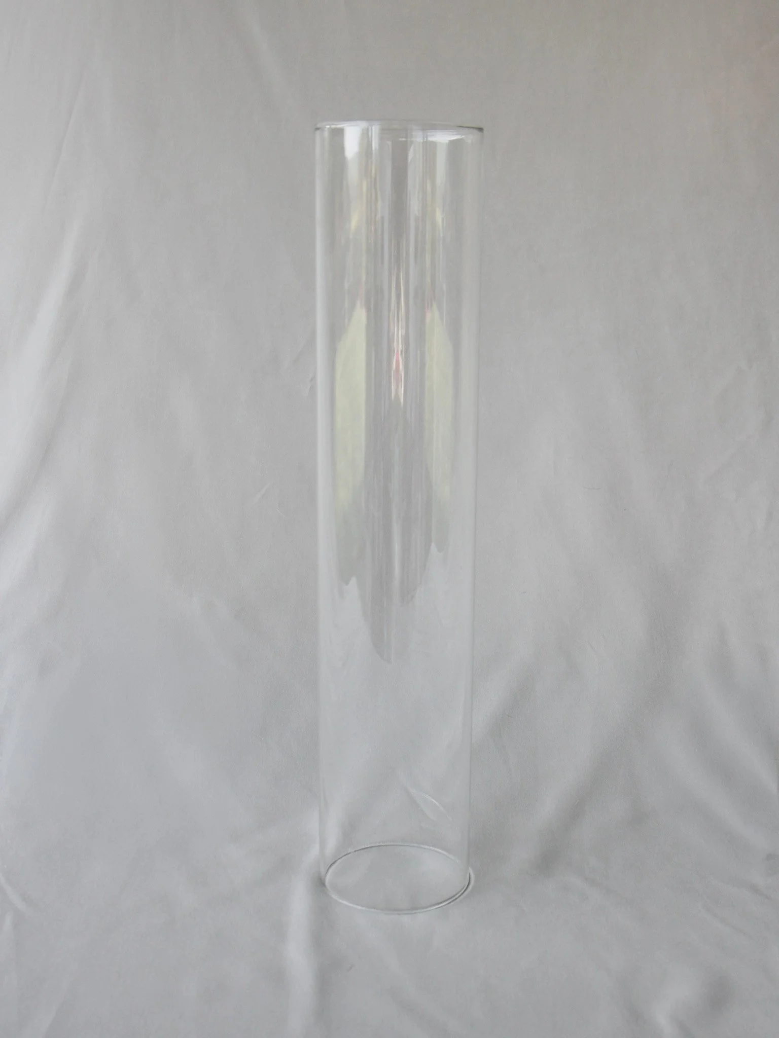 A tall, clear glass tube standing upright on a white surface with a plain background.