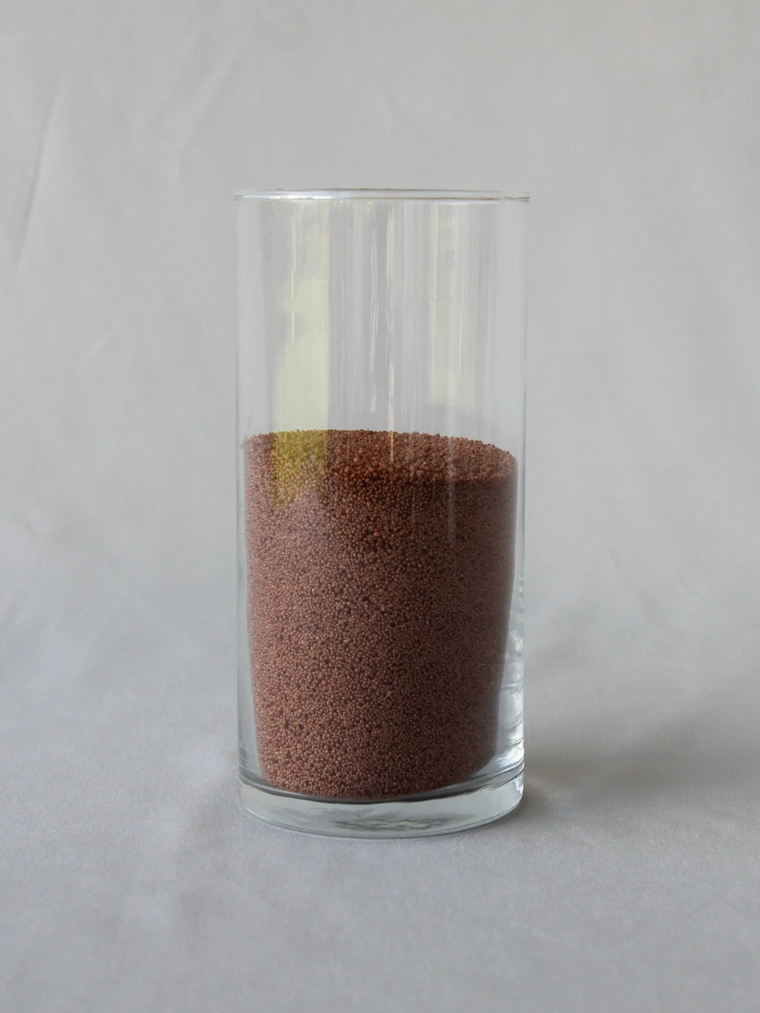 A clear glass containing pink sand, set against a plain white background.