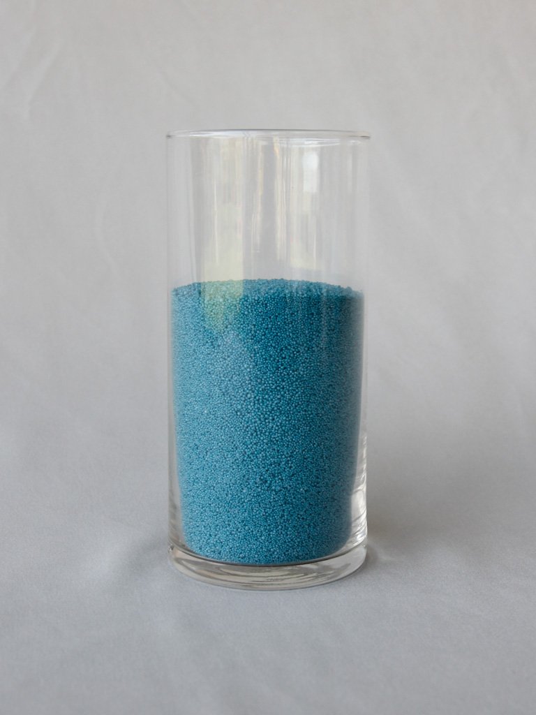 A clear glass container filled with small blue granular beads.