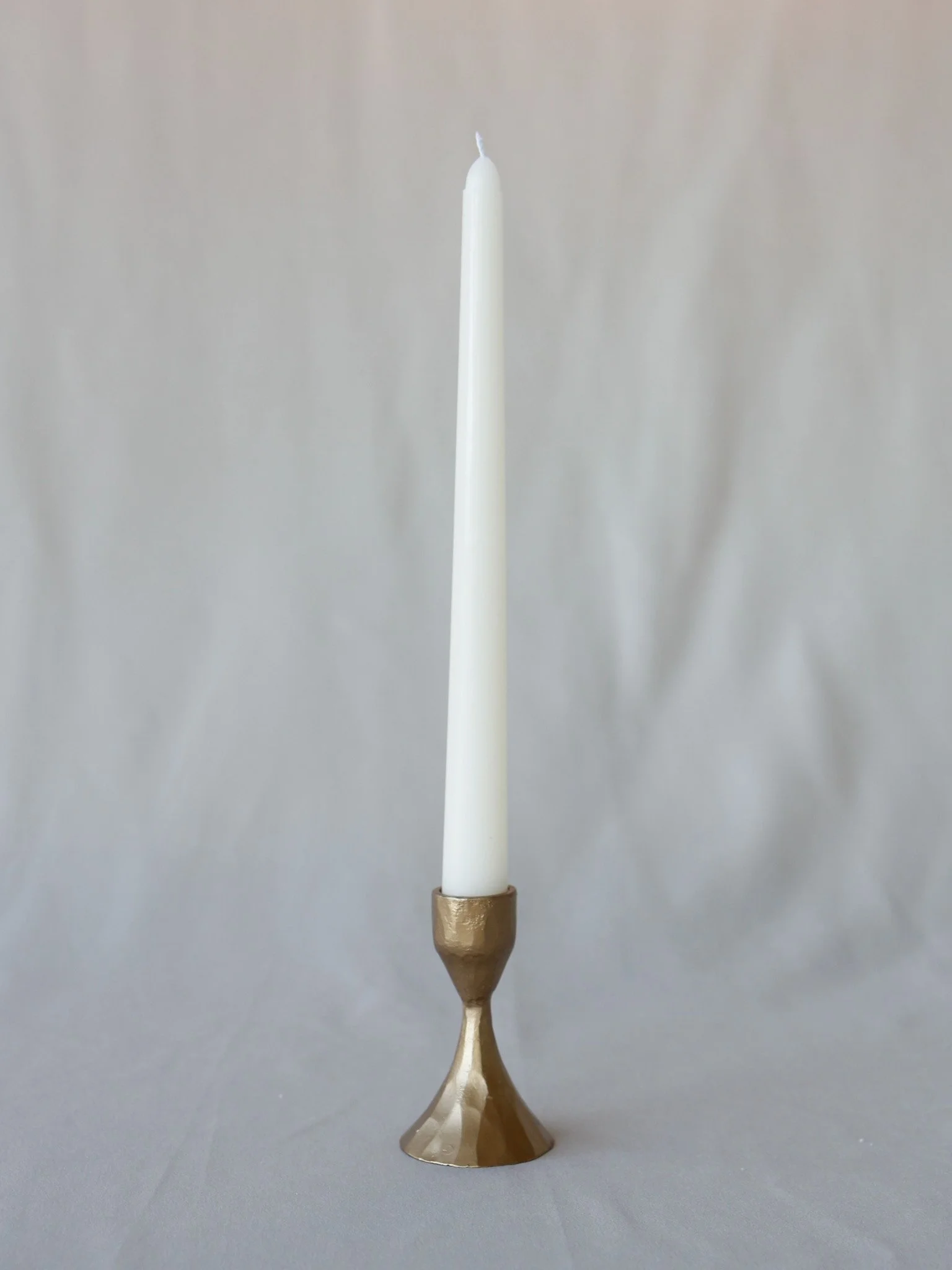 White candle in a gold-colored candle holder against a plain gray background.