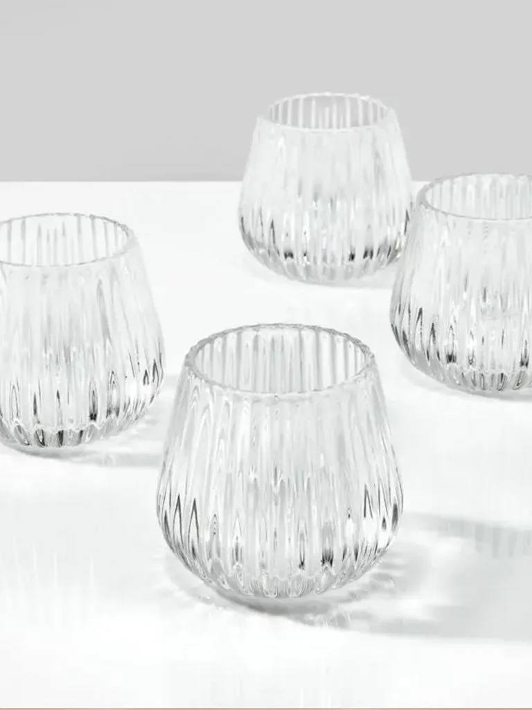 Four clear, ribbed glass cups placed on a white surface against a light gray background.