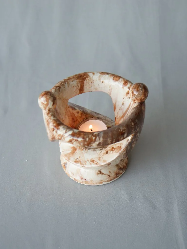 A stone candle holder with a tealight candle inside on a light gray surface.
