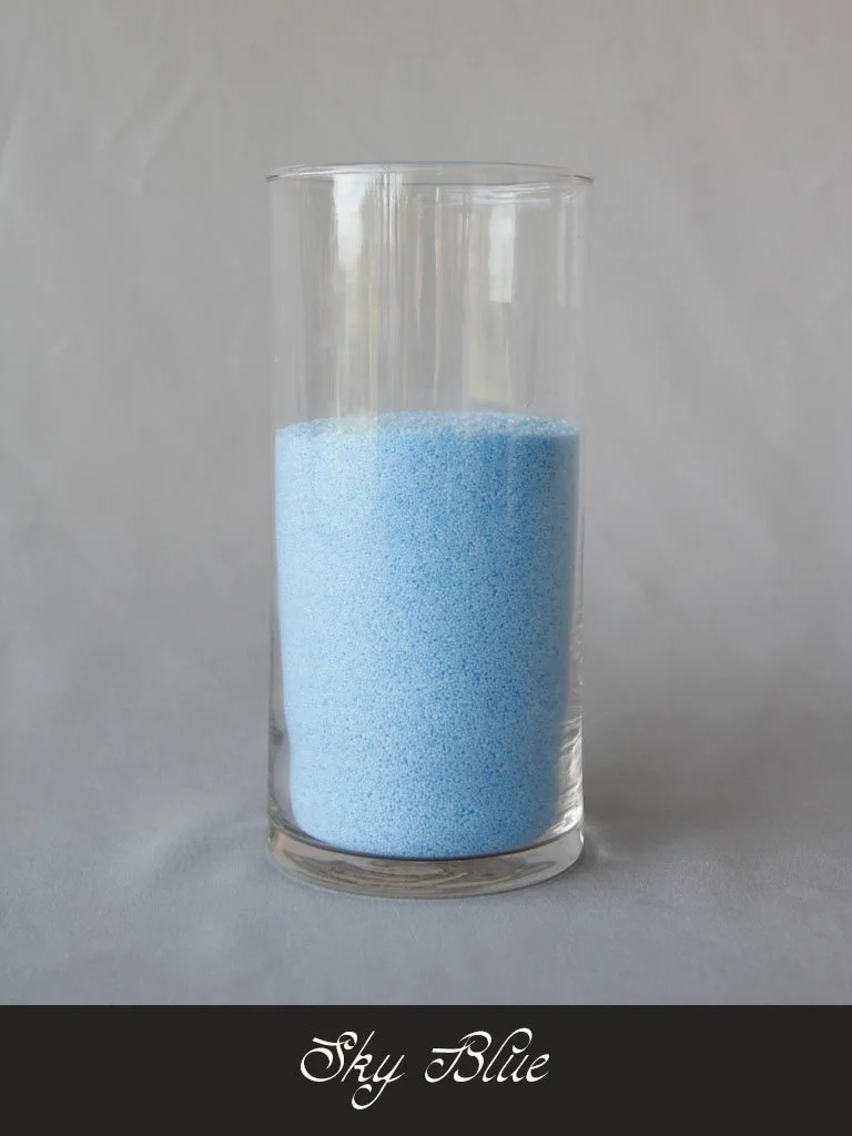 A clear glass filled with sky blue sand or small granules against a plain background. The text "Sky Blue" appears at the bottom of the image.