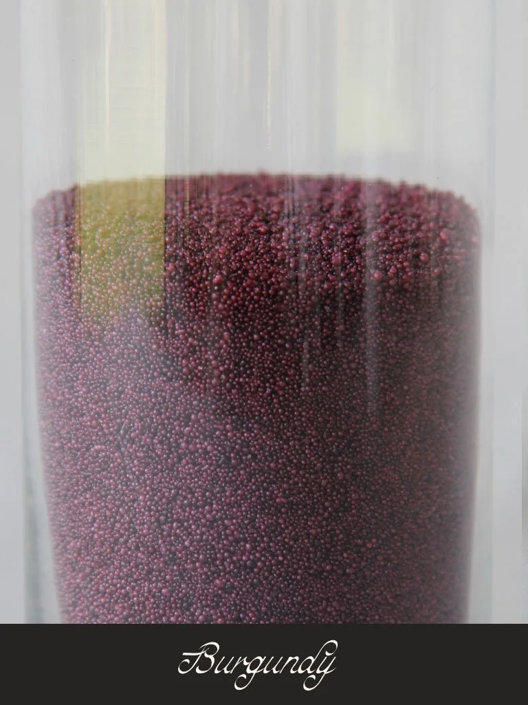 Close-up of a glass container filled with burgundy-colored small spherical beads or seeds, with the word 'Burgundy' written at the bottom.