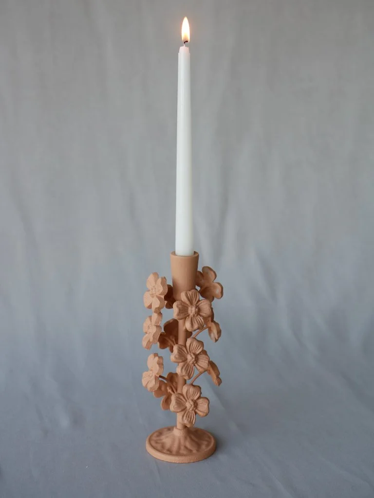 A tall white candle in a decorative beige ceramic holder adorned with detailed beige flower designs.