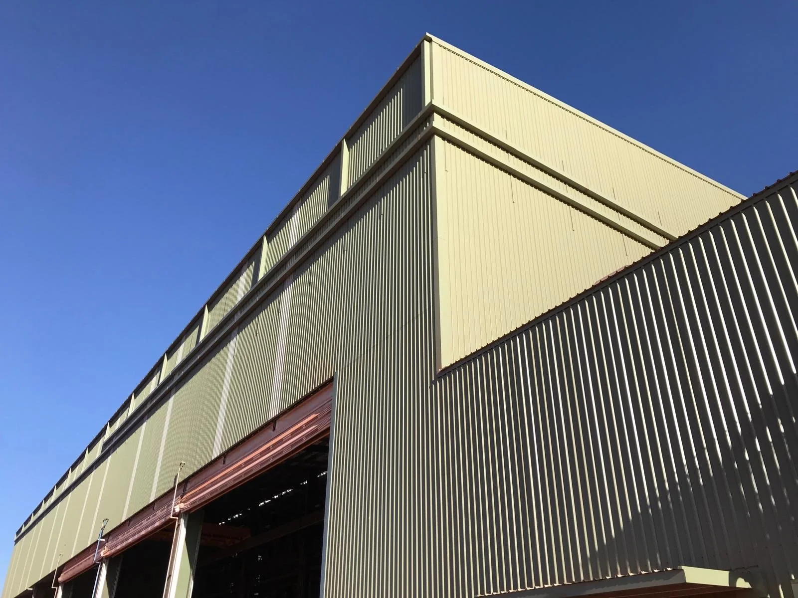 Close-up of a large industrial warehouse or factory building with ribbed metal siding, under a clear blue sky.
