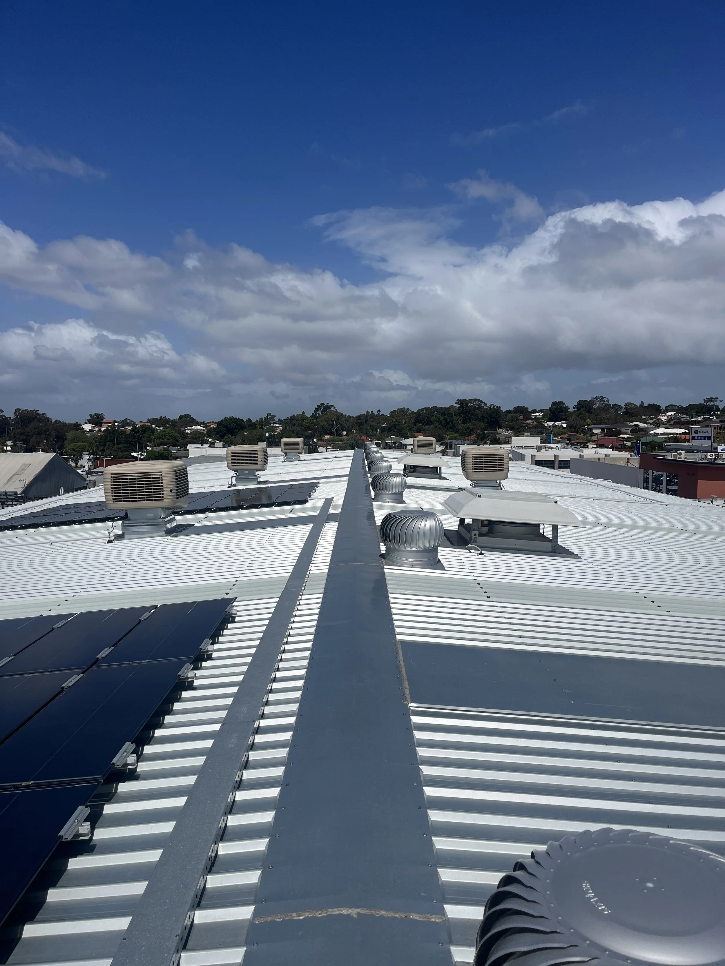 View of a metal rooftop with multiple HVAC units and solar panels, under a partly cloudy sky.