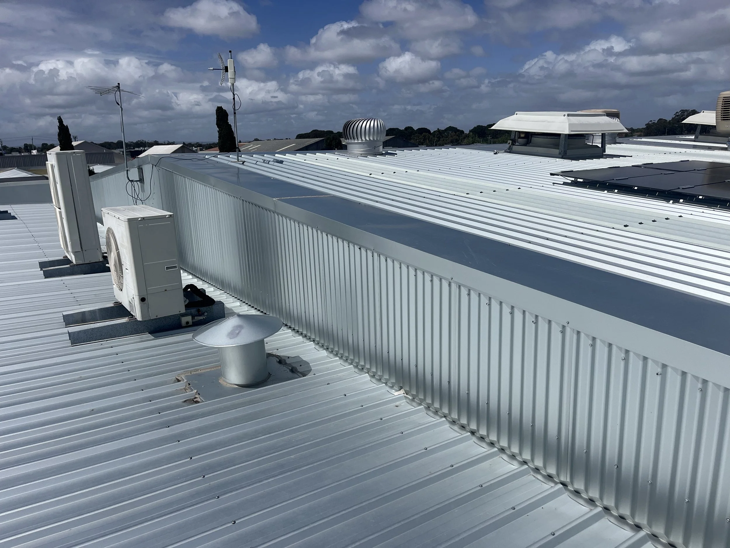 A metal rooftop with air conditioning units, vents, and antennas under a partly cloudy sky.