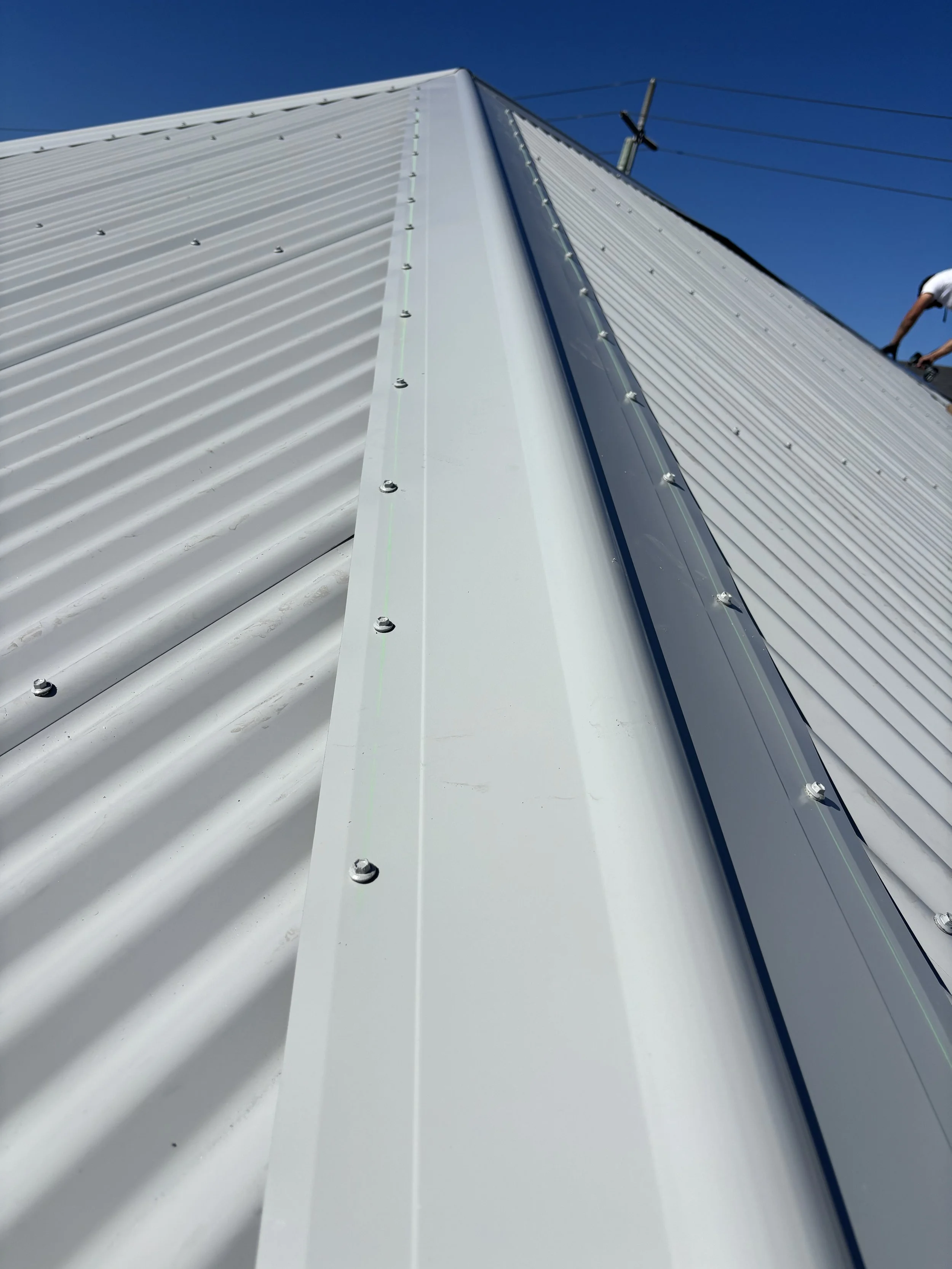 Close-up view of a metal roof with bolts, showing the edge and part of the roof structure, under a clear blue sky.