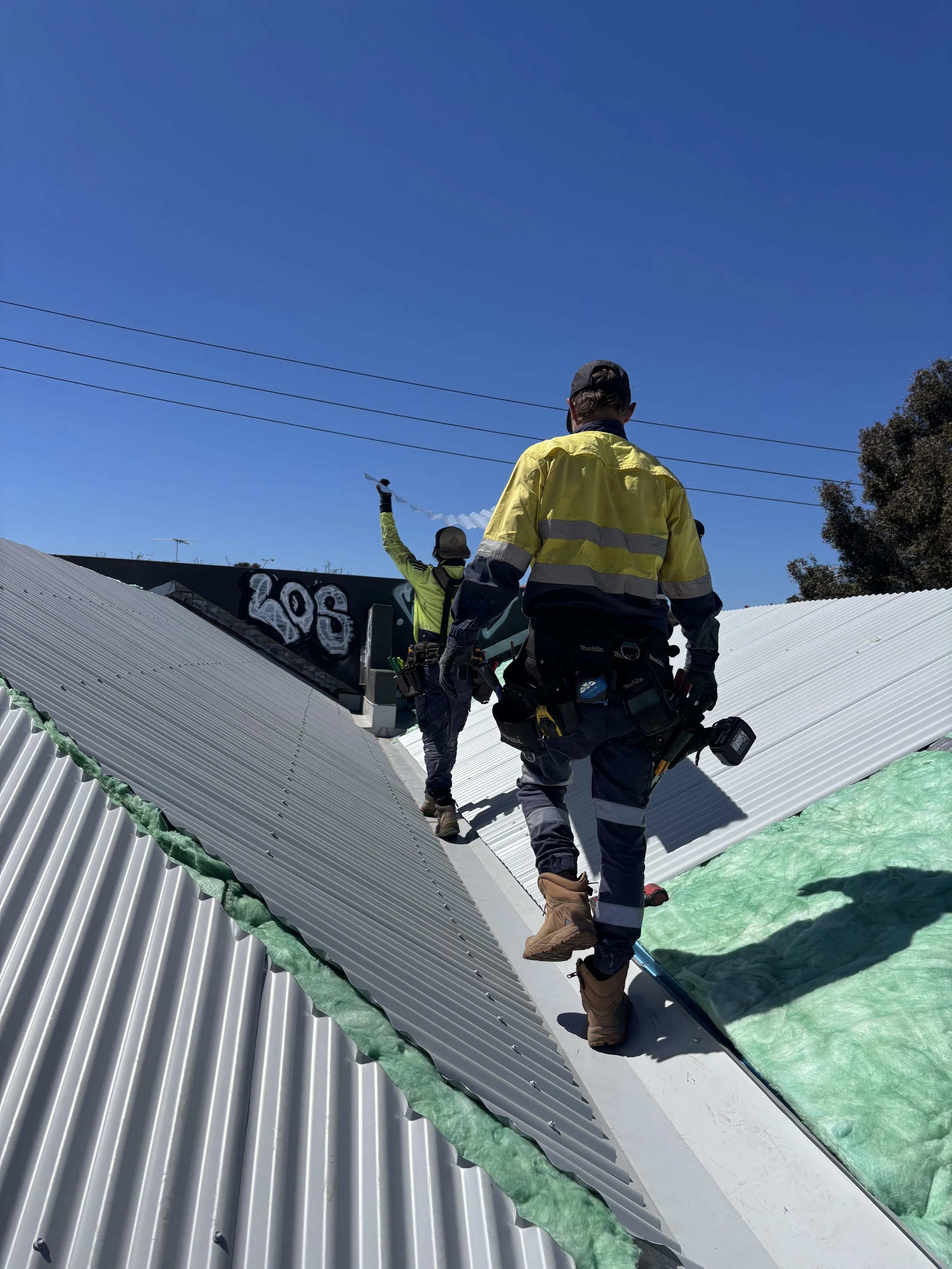 Construction workers installing or repairing metal roofing on a building under a clear blue sky.