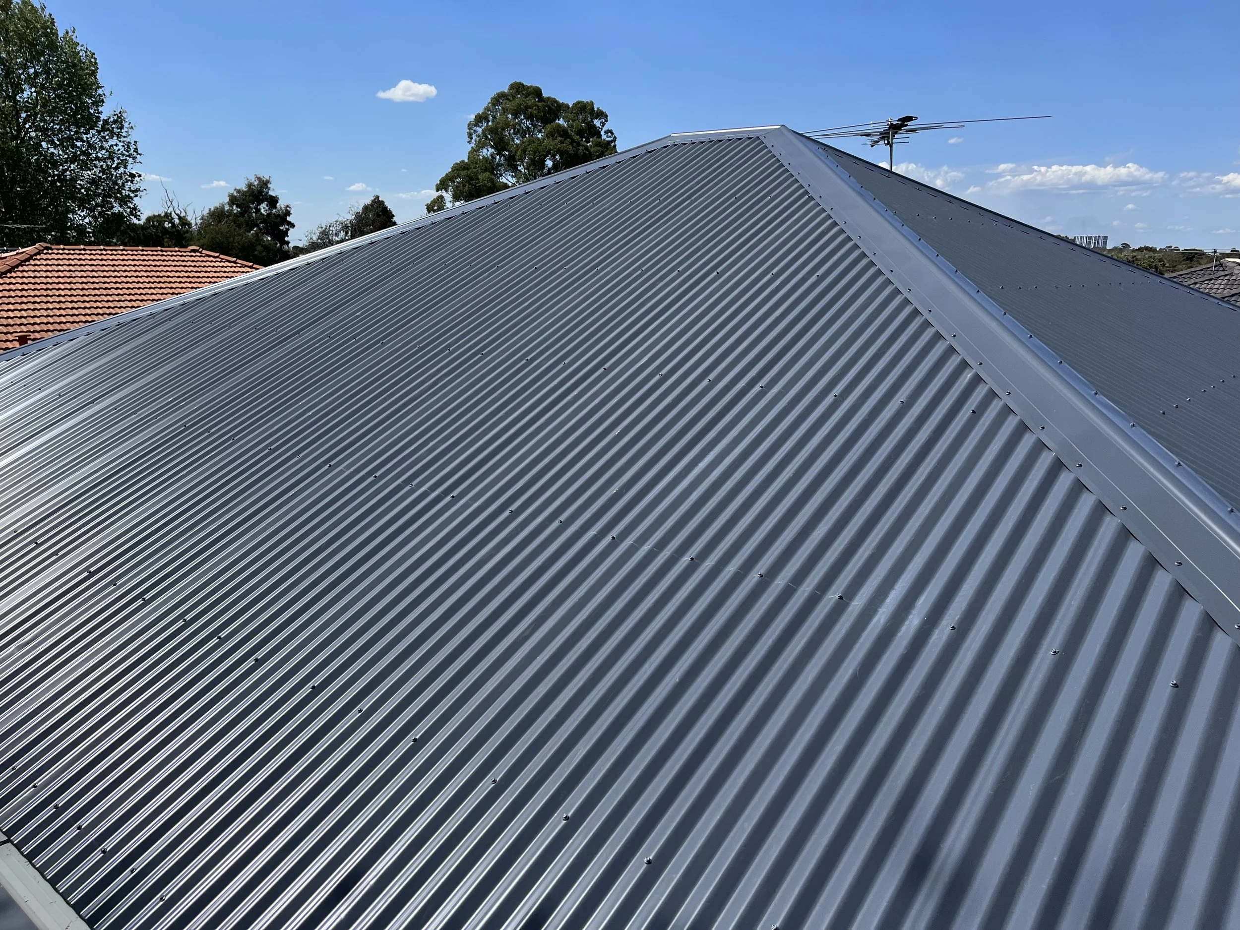 A metal roof with evenly spaced ridges, gray in color, under a clear blue sky with a few clouds.