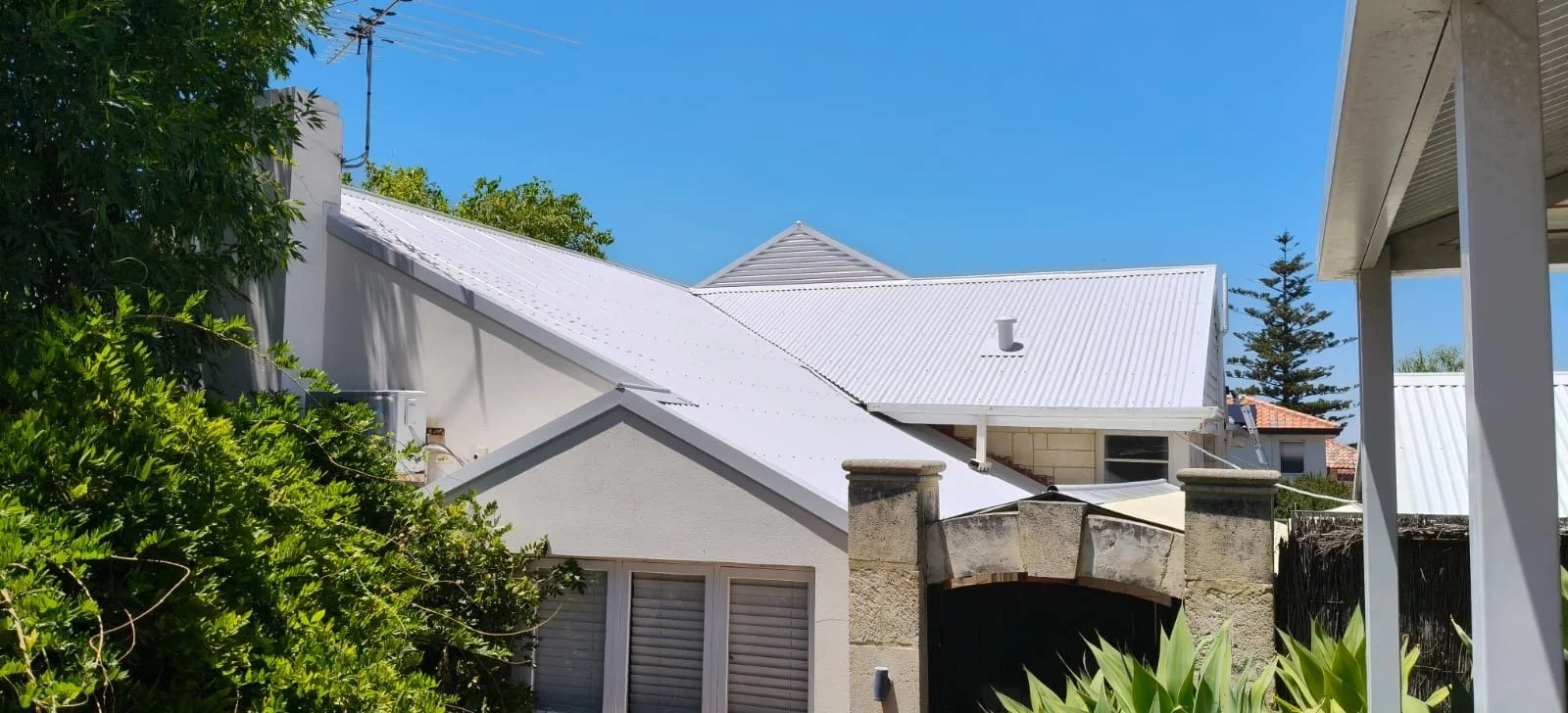 White metal roofs on houses with greenery and a blue sky in the background.