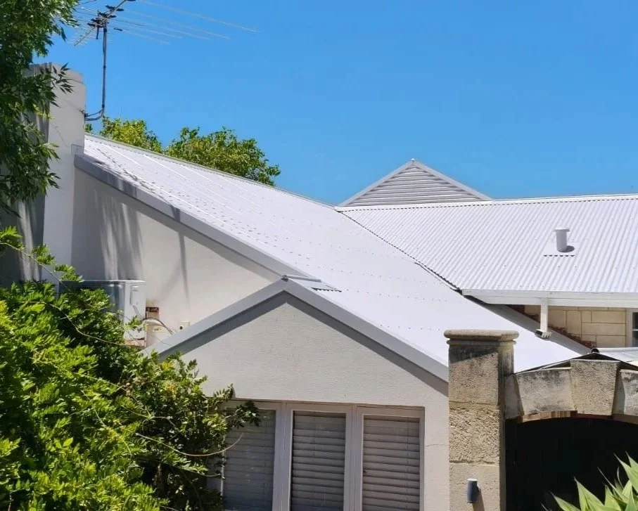 Close-up of white metal roofs on residential houses with blue sky and green tree branches in the background.