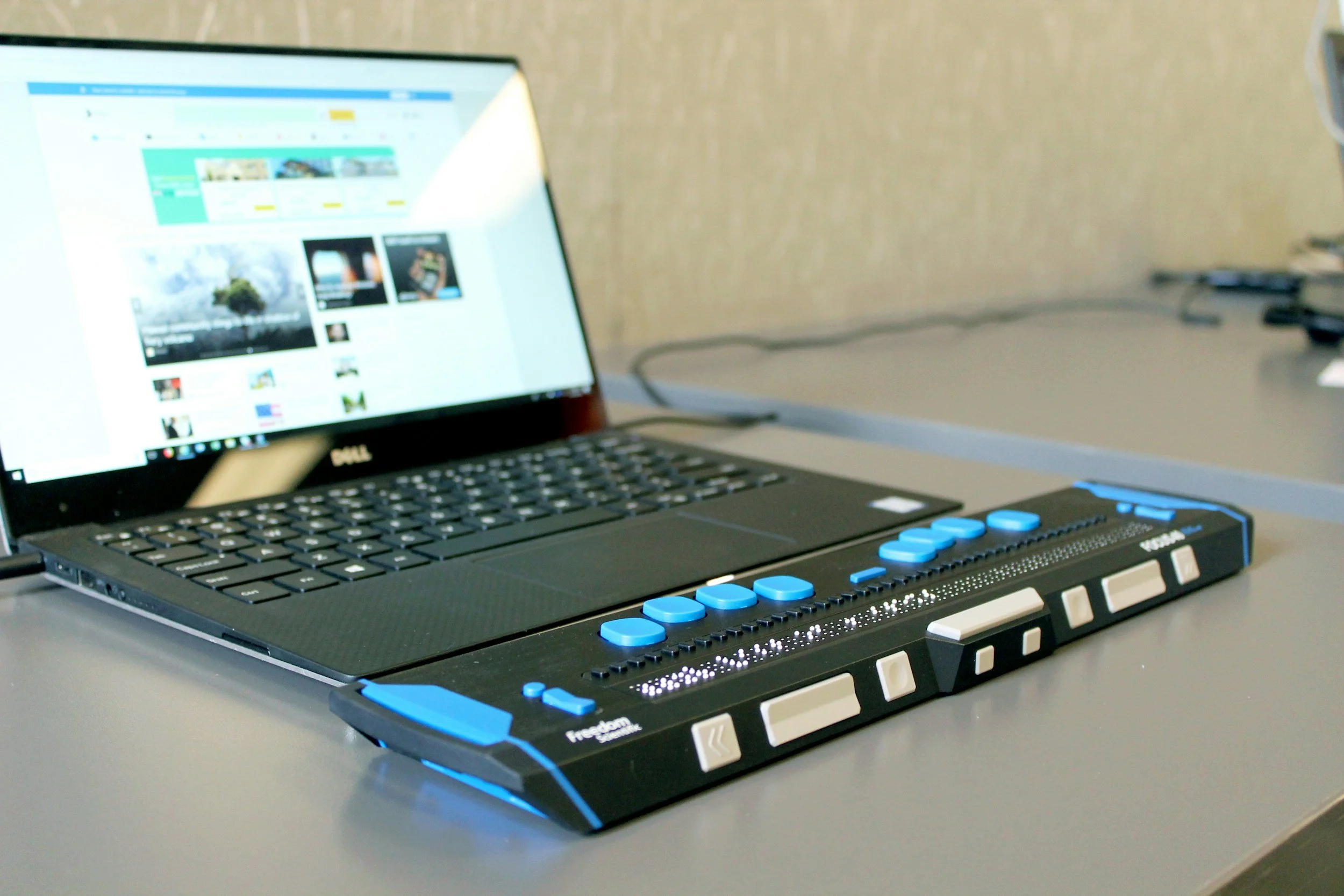 This is an image of a laptop with a black and blue braille display in front of it.