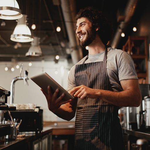 This is an image to represent restaurant staff. It is an image of a man holding a tablet. He is wearing an apron and smiling from ear to ear.