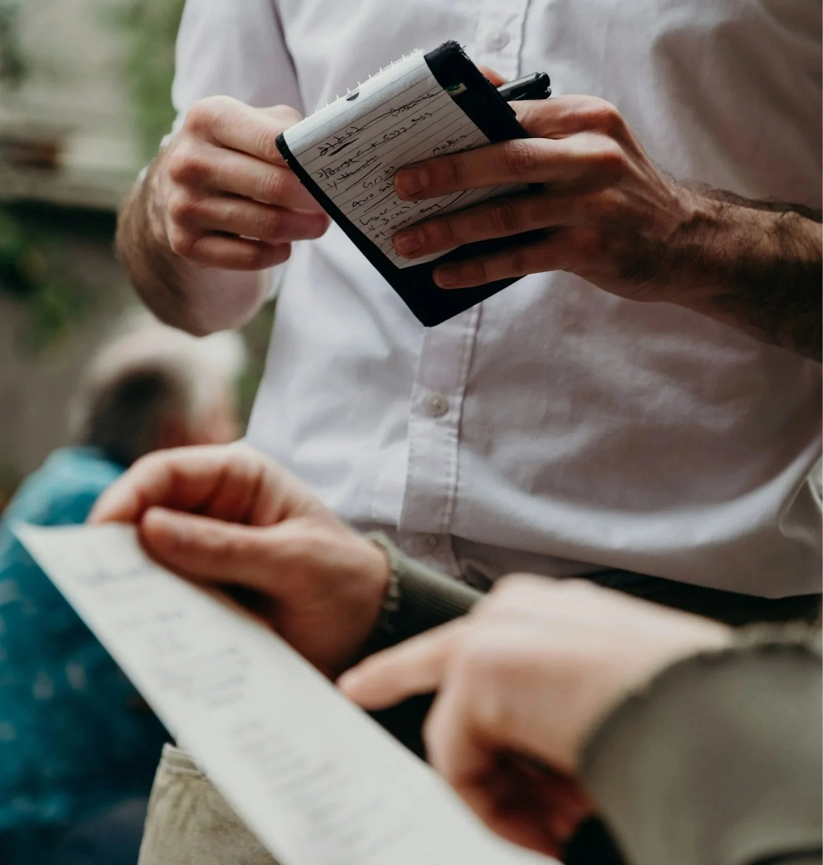 This is an image of two folks seemingly talking. One person is holding a notebook, while the other holds what looks to be a receipt.