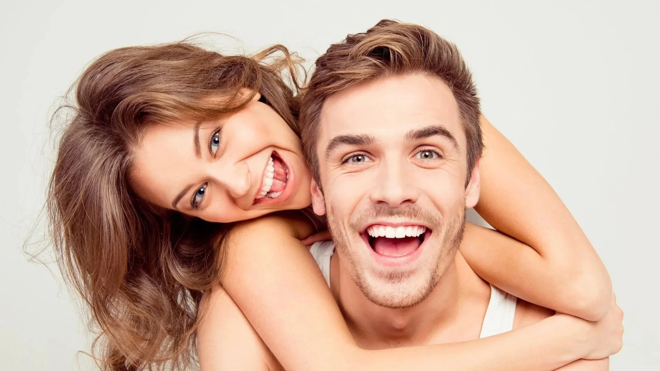 A smiling woman piggyback riding on a smiling man against a plain background, as a reflection of relationship property agreements and matters.