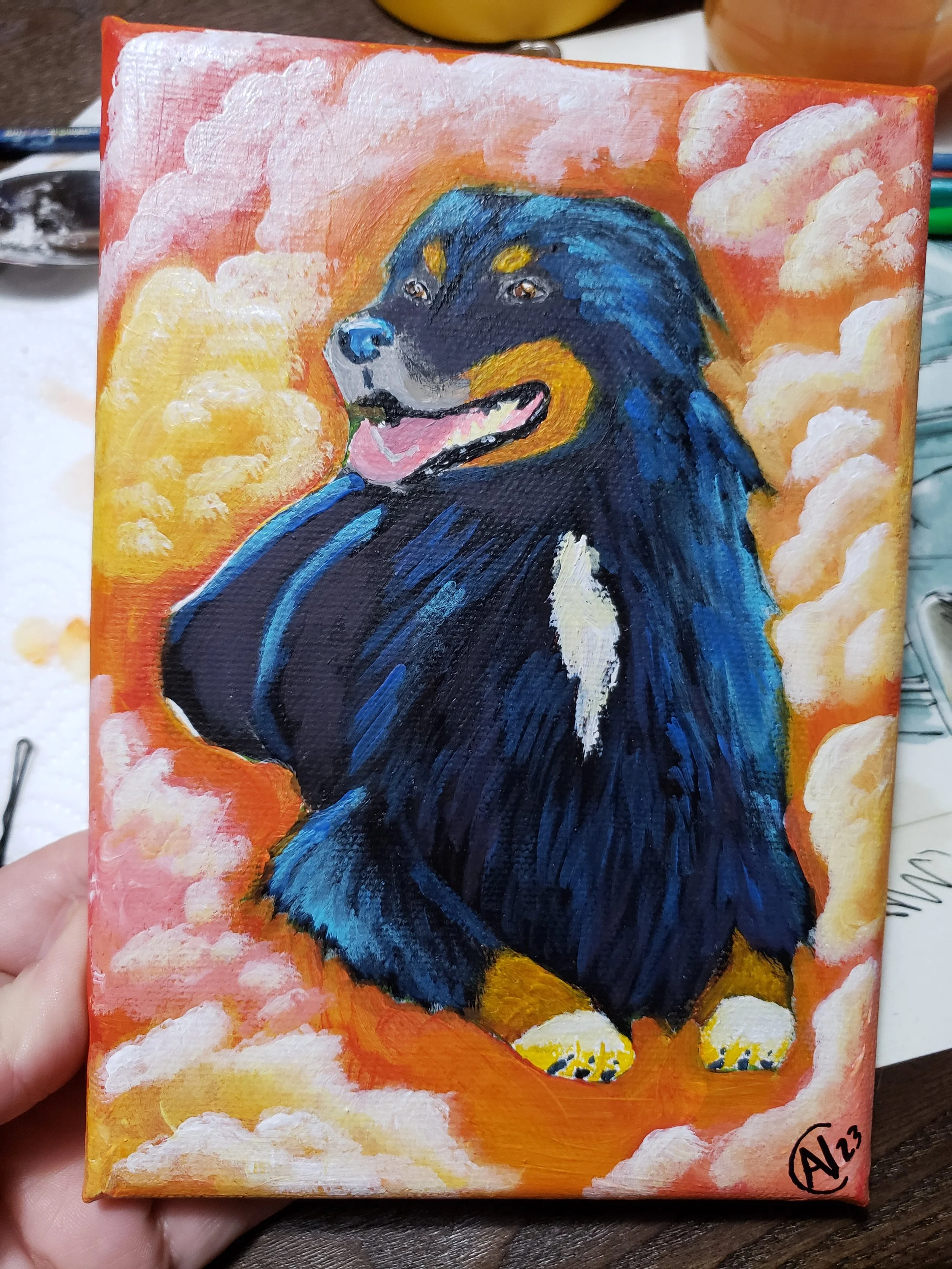 A colorful painting of a happy black and tan dog with blue fur accents, sitting among fluffy orange and yellow clouds.