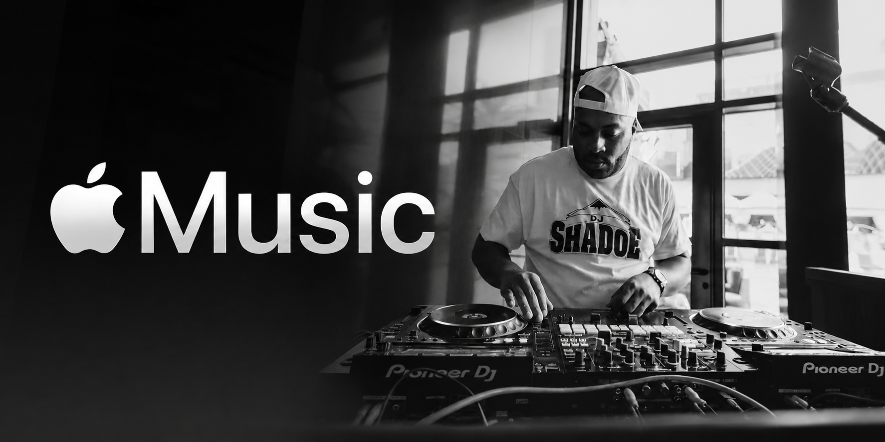 A DJ performing on a DJ booth with Apple Music logo in the background, in a black and white photo.