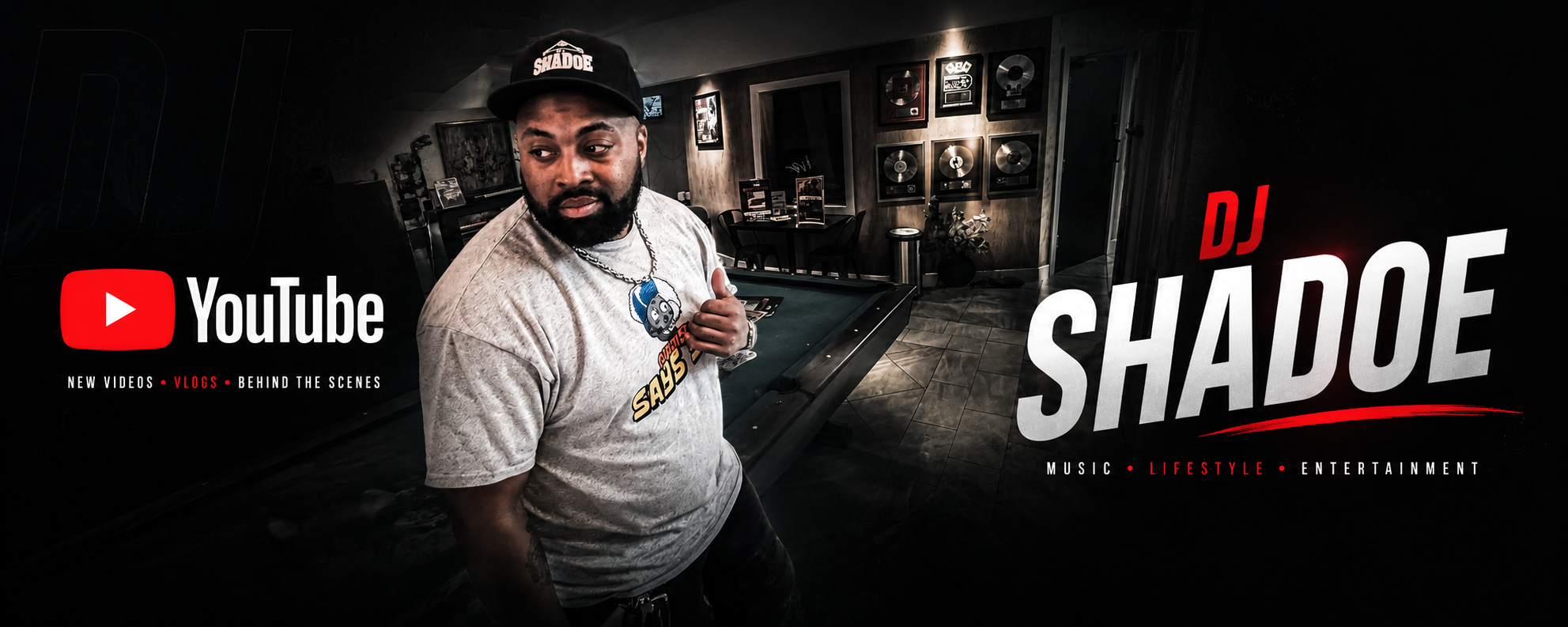 A man wearing a black cap with 'SHADOE' written on it, a gray t-shirt with a graphic of a face, and a silver chain necklace, standing in a dimly lit room with framed awards and artworks on the wall, in front of a pool table, with a YouTube logo and the text 'DJ SHADOE' and 'NEW VIDEOS, VLOGS, BEHIND THE SCENES, MUSIC, LIFESTYLE, ENTERTAINMENT'.