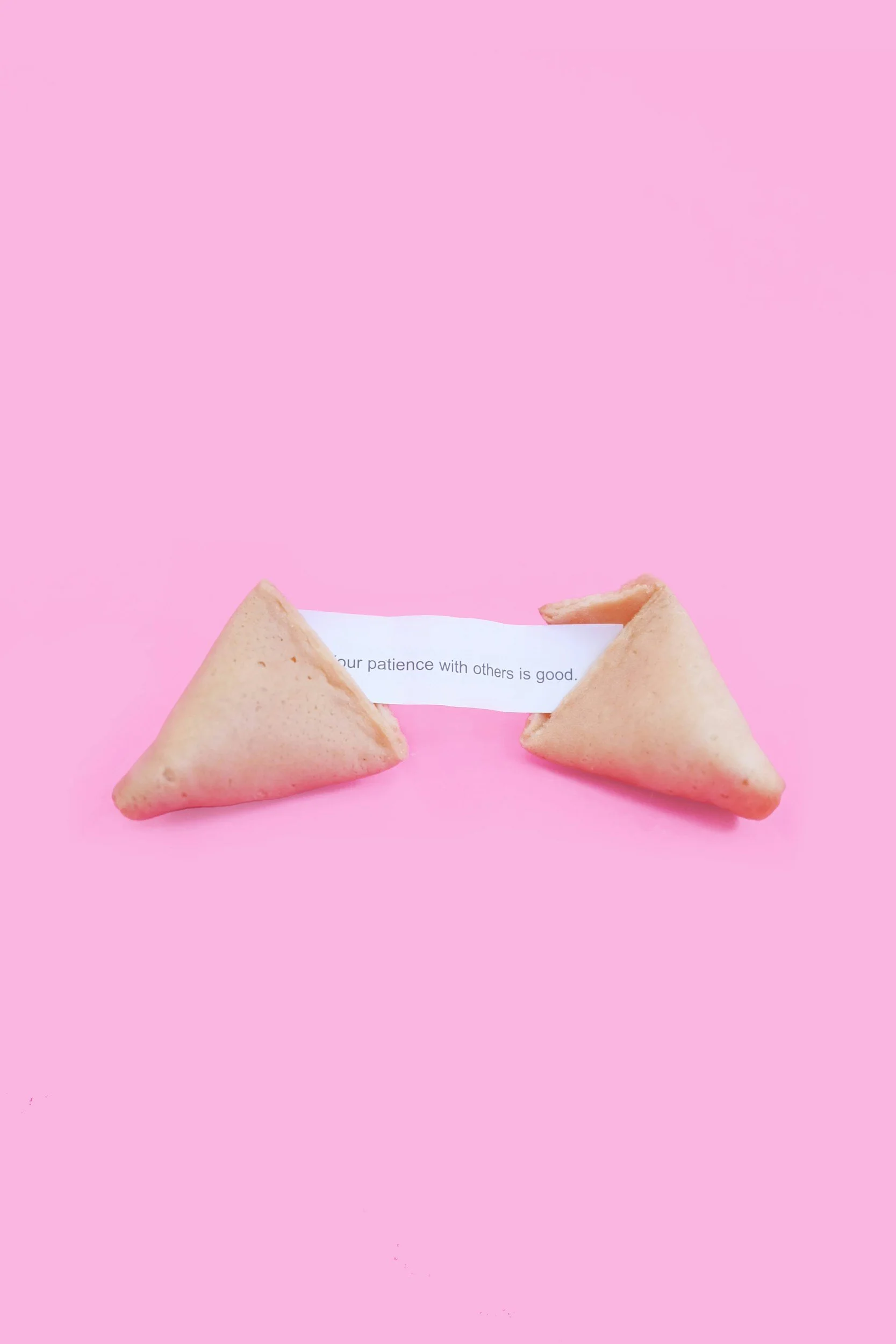 Two fortune cookies on a pink background, connected by a strip of paper reading, "your patience with others is good."