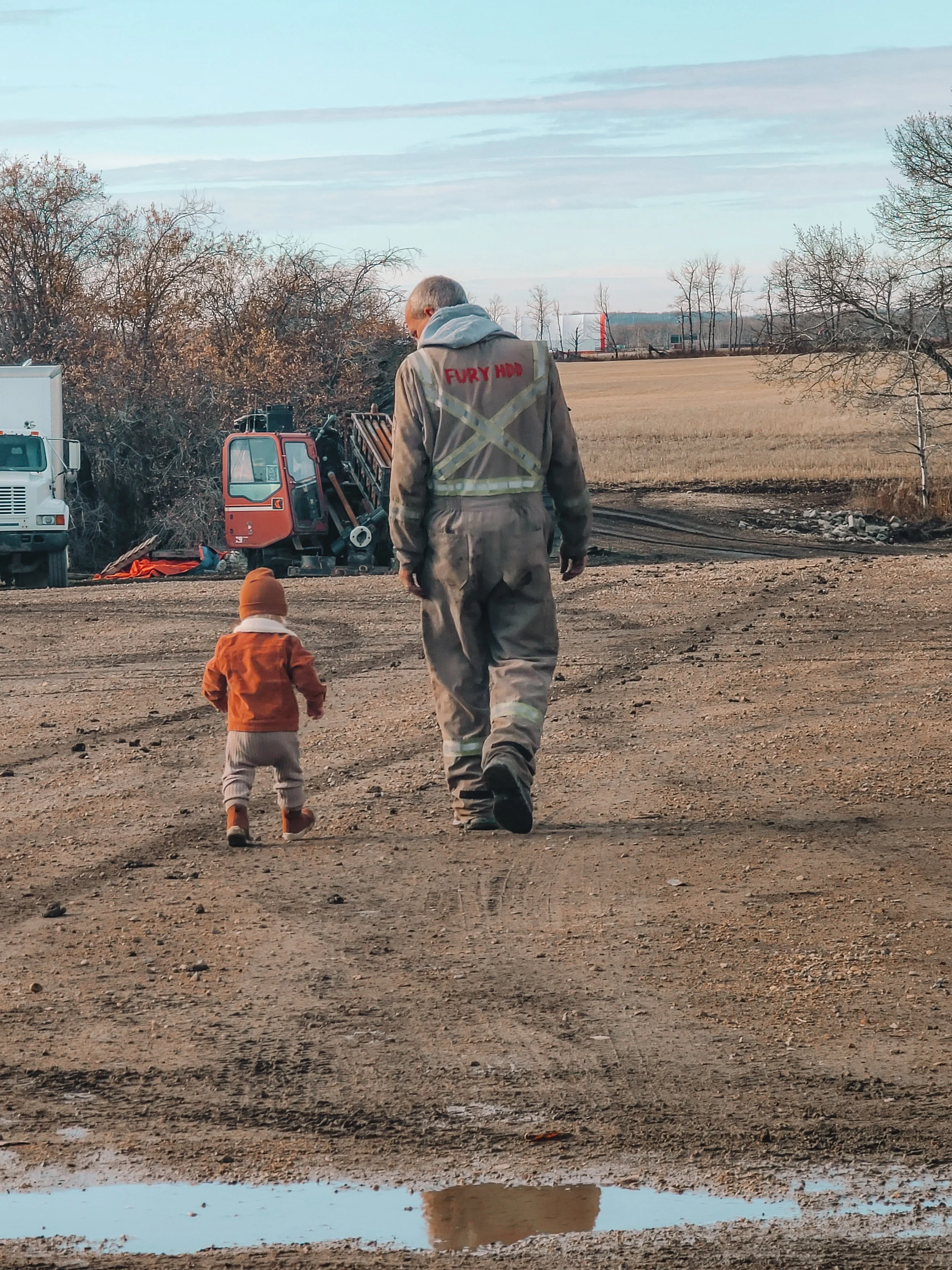 Company Owner walking with his grandson on a dirt path with construction equipment and trees in the background.