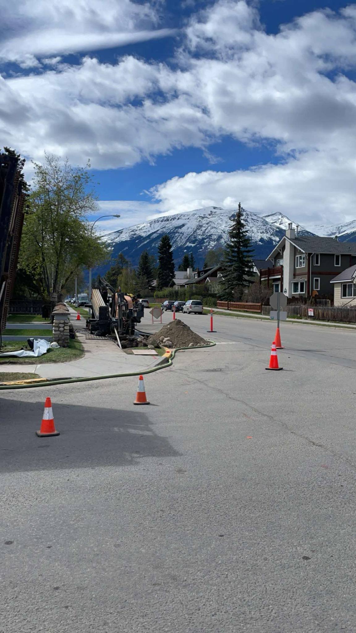 Street with construction cones and equipment, with snow-capped mountains and a partly cloudy sky in the background. Jasper, Alberta