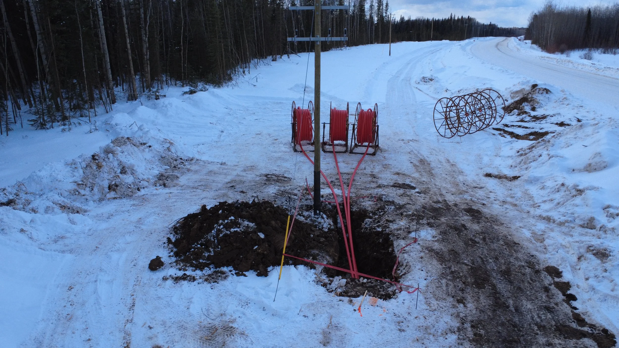Electrical wiring installation in snowy outdoor area with snow-covered road and forest background.