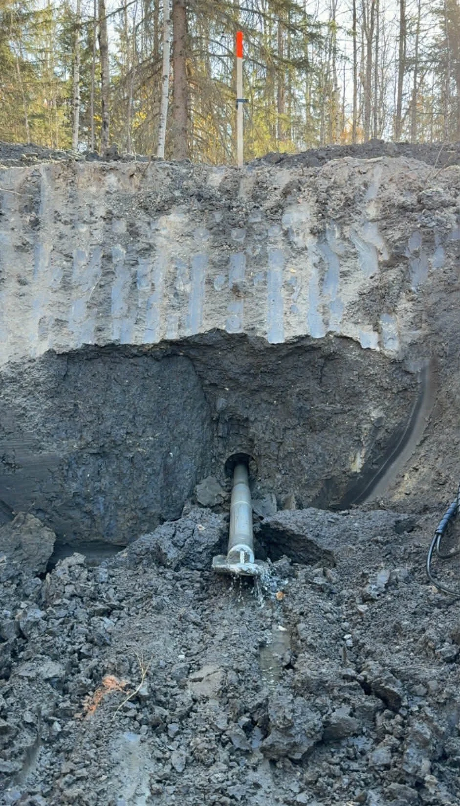 Underground pipe installation with excavation site and soil layers visible, trees in the background.
