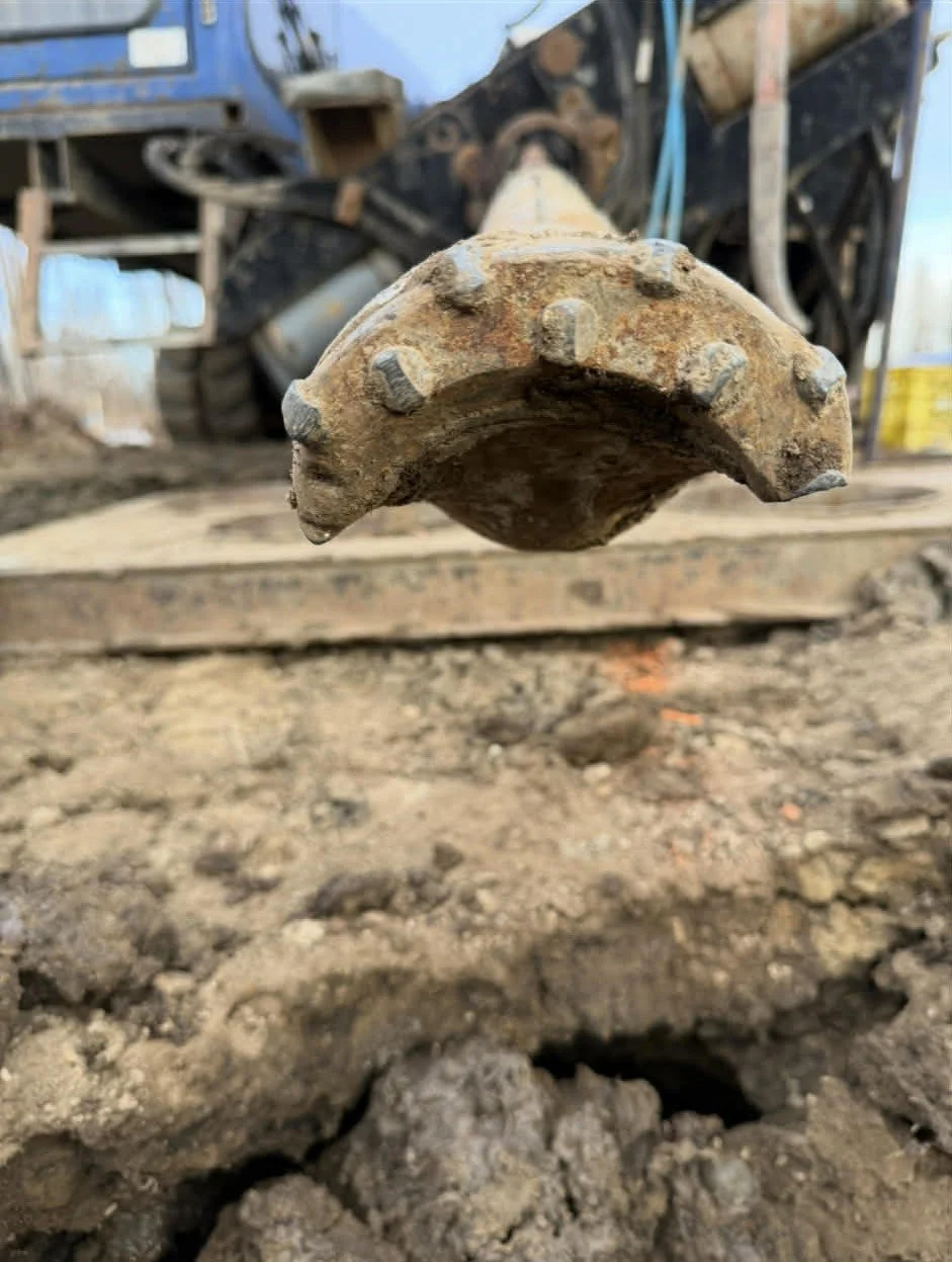 Close-up of a digging machine's metal digging bucket, suspended above muddy ground at a construction site.