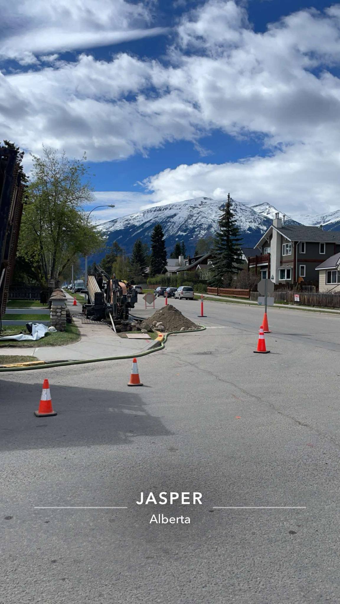 Street construction in Jasper, Alberta with construction cones, equipment, and a view of snow-capped mountains in the background.