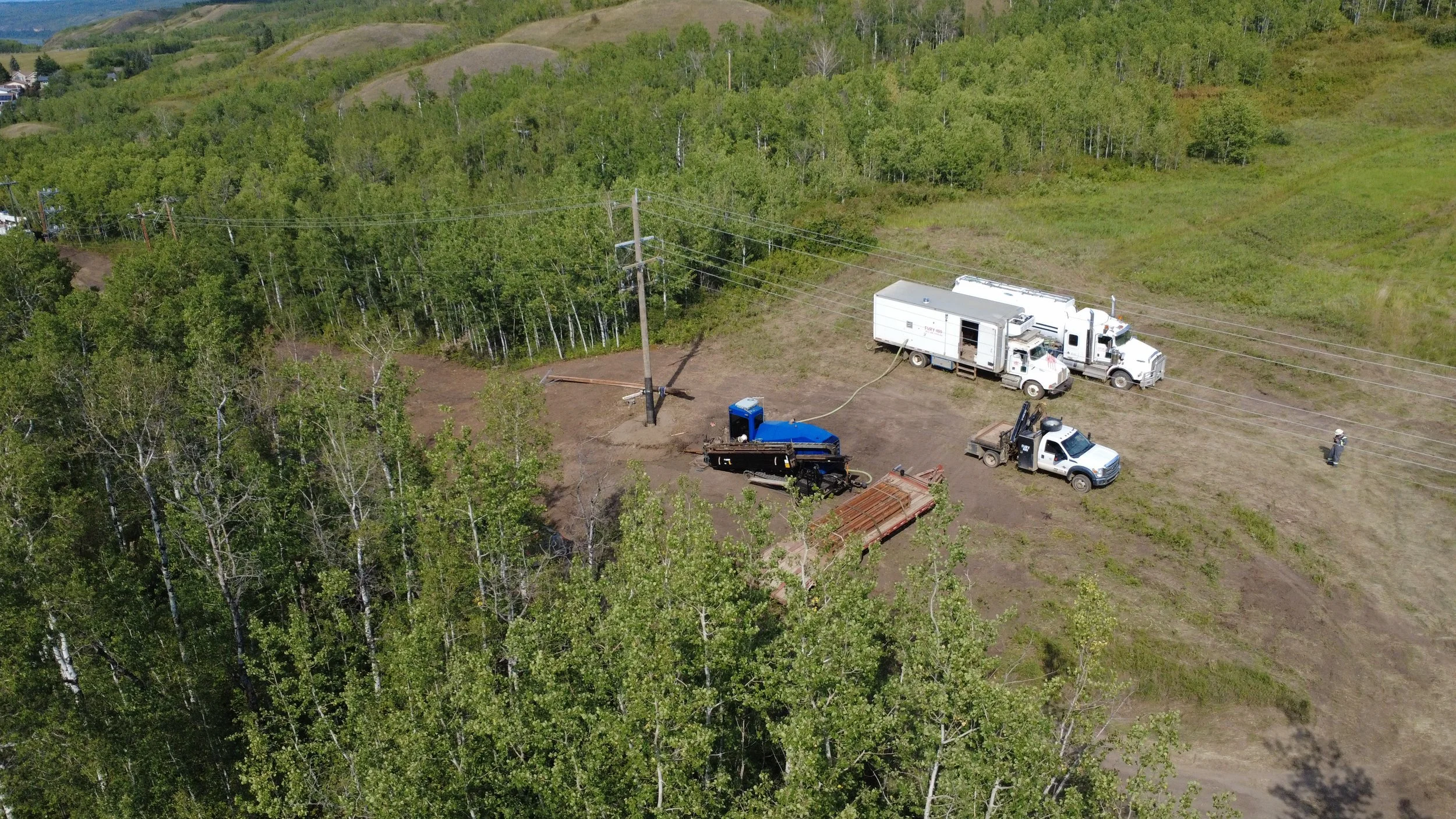Aerial view of a work site in a forested area with trucks, a portable toilet, and construction equipment.