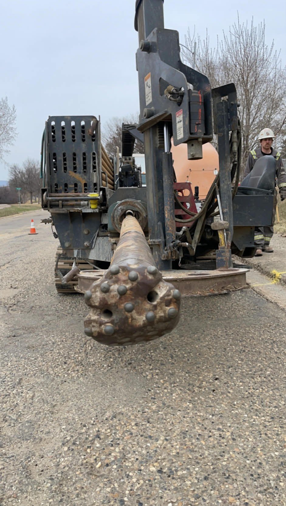 Close-up of a tracked drilling machine on the road with a worker in safety gear standing nearby.