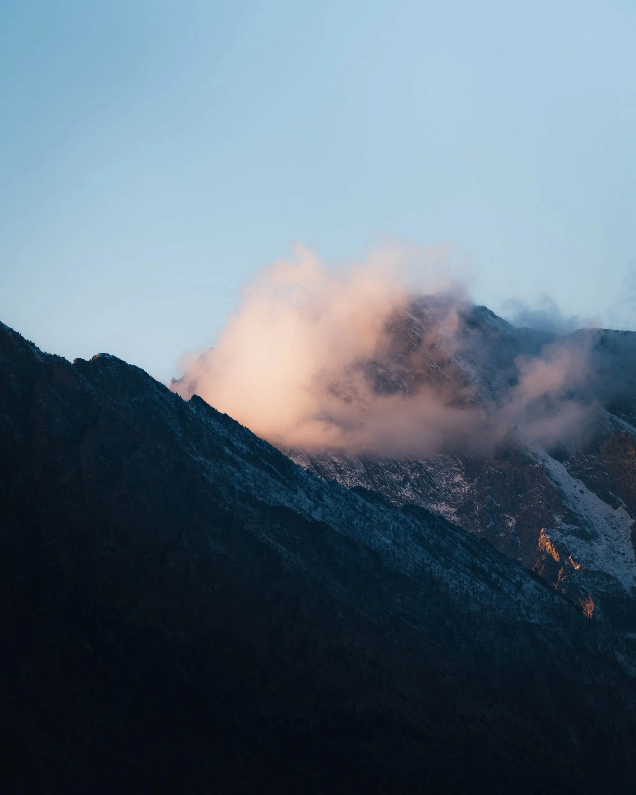 Sunlit mountain peaks with partly cloudy sky during sunset.
