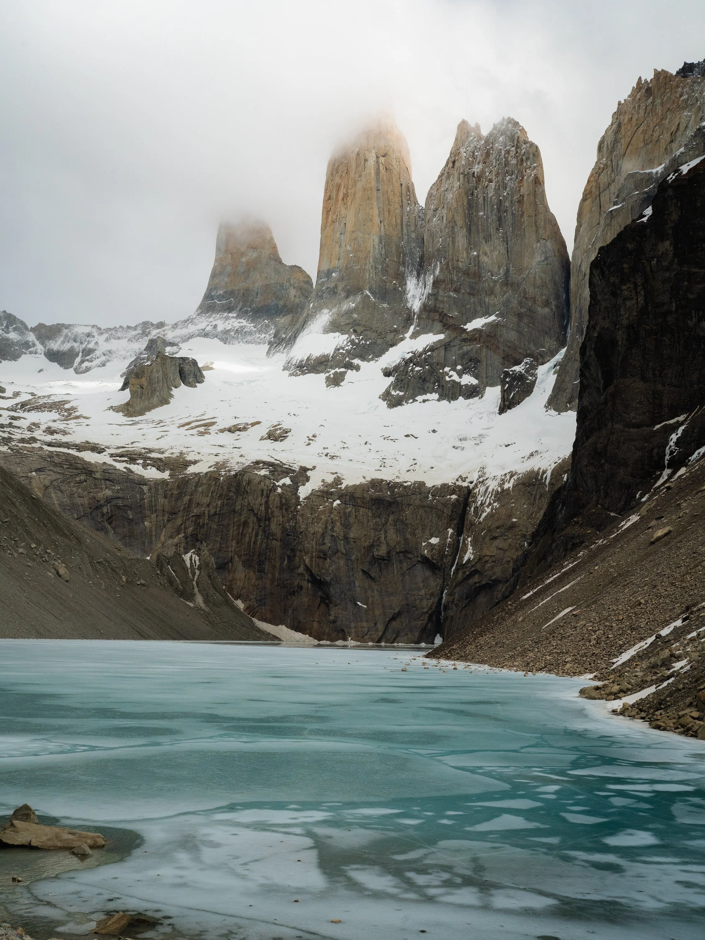 Snow-capped Torres del Paine mountains surrounding an icy lake in a mountainous landscape.