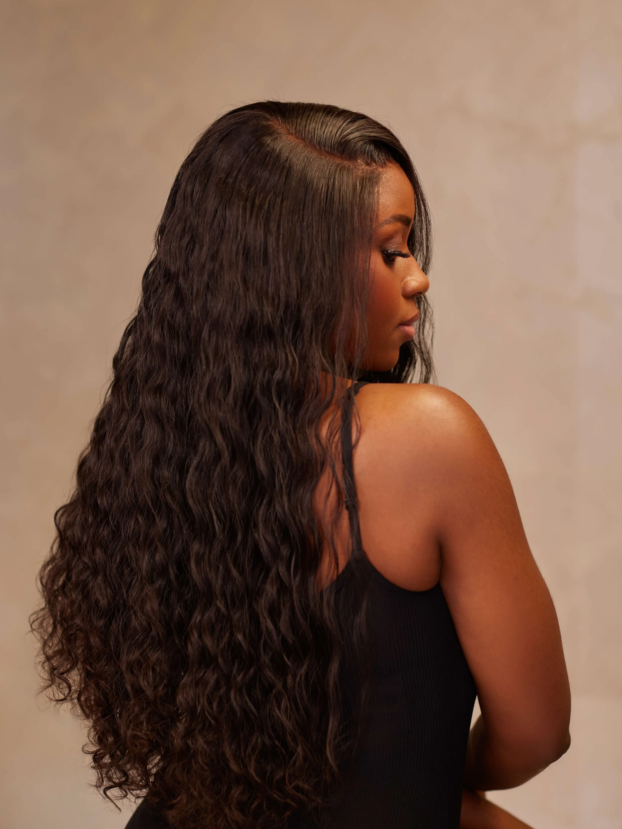 A woman with long, wavy dark hair and a side profile, wearing a black sleeveless top.